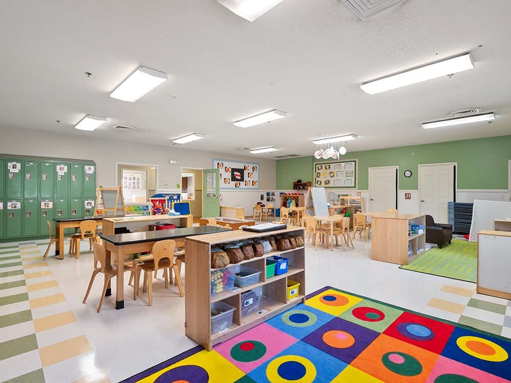 Classroom with tables, chairs, green lockers, and a colorful rug