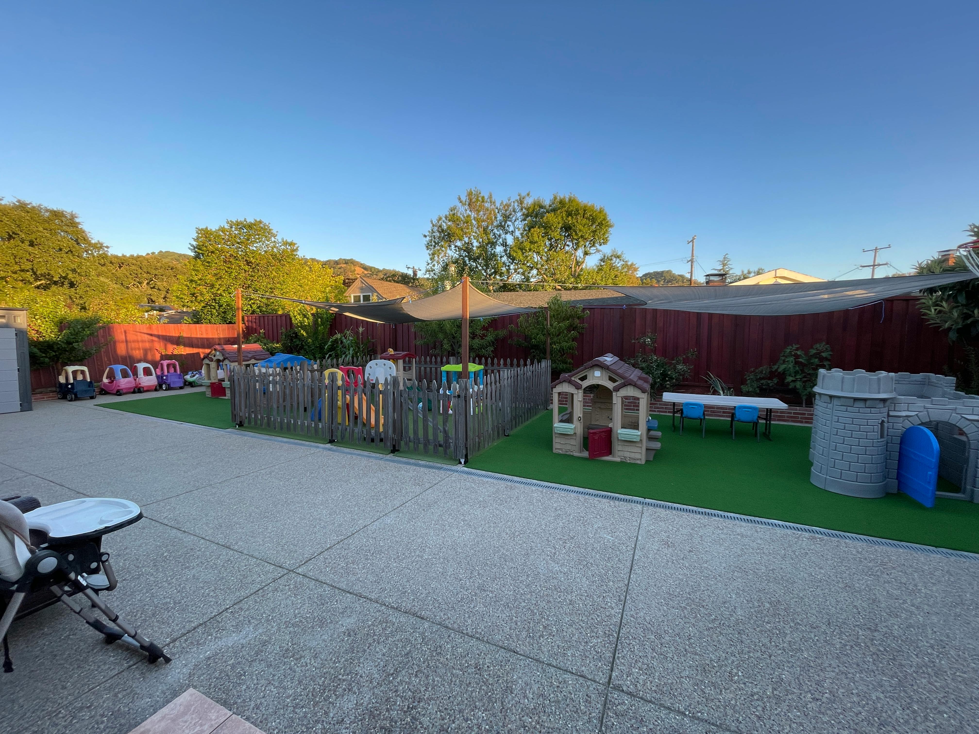Outdoor play area with a small fence, playhouse, and ride-on toys