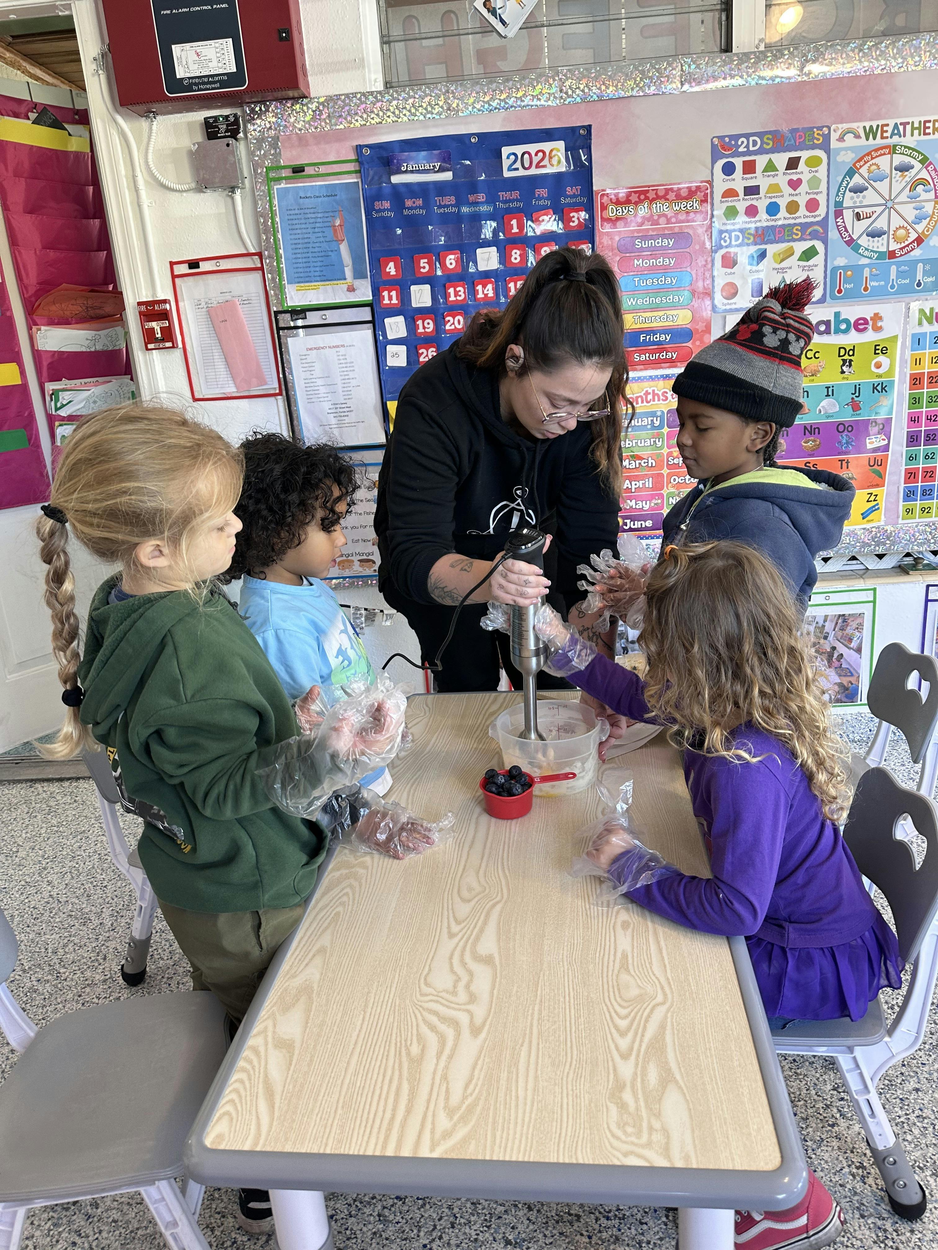 Adult using immersion blender while children in plastic gloves watch