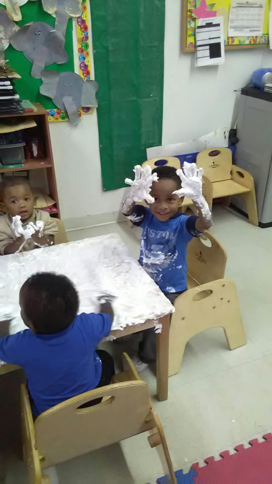 Three children playing with shaving cream at a table in a classroom