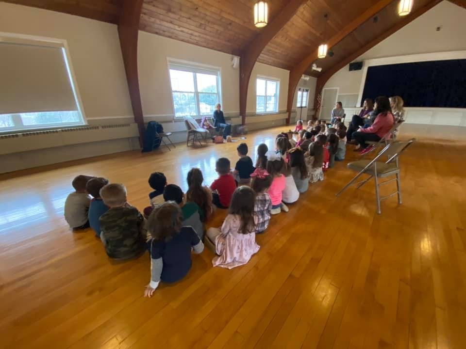 Children sitting on a wooden floor in a large room