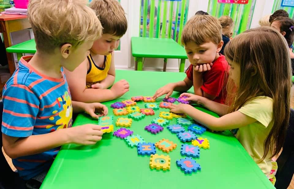 Children playing with colorful puzzle pieces at a green table