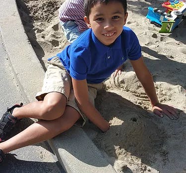 Child in blue shirt playing in sand