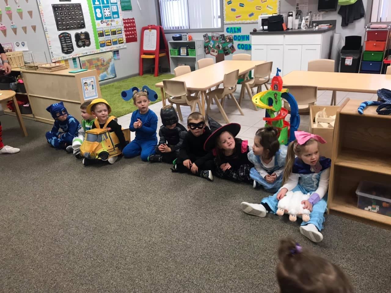 Children in costumes sitting on the floor in a classroom