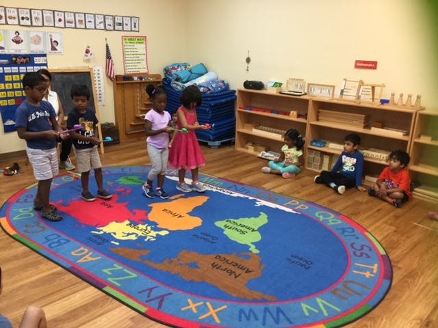 Children standing and sitting on a world map rug in a classroom