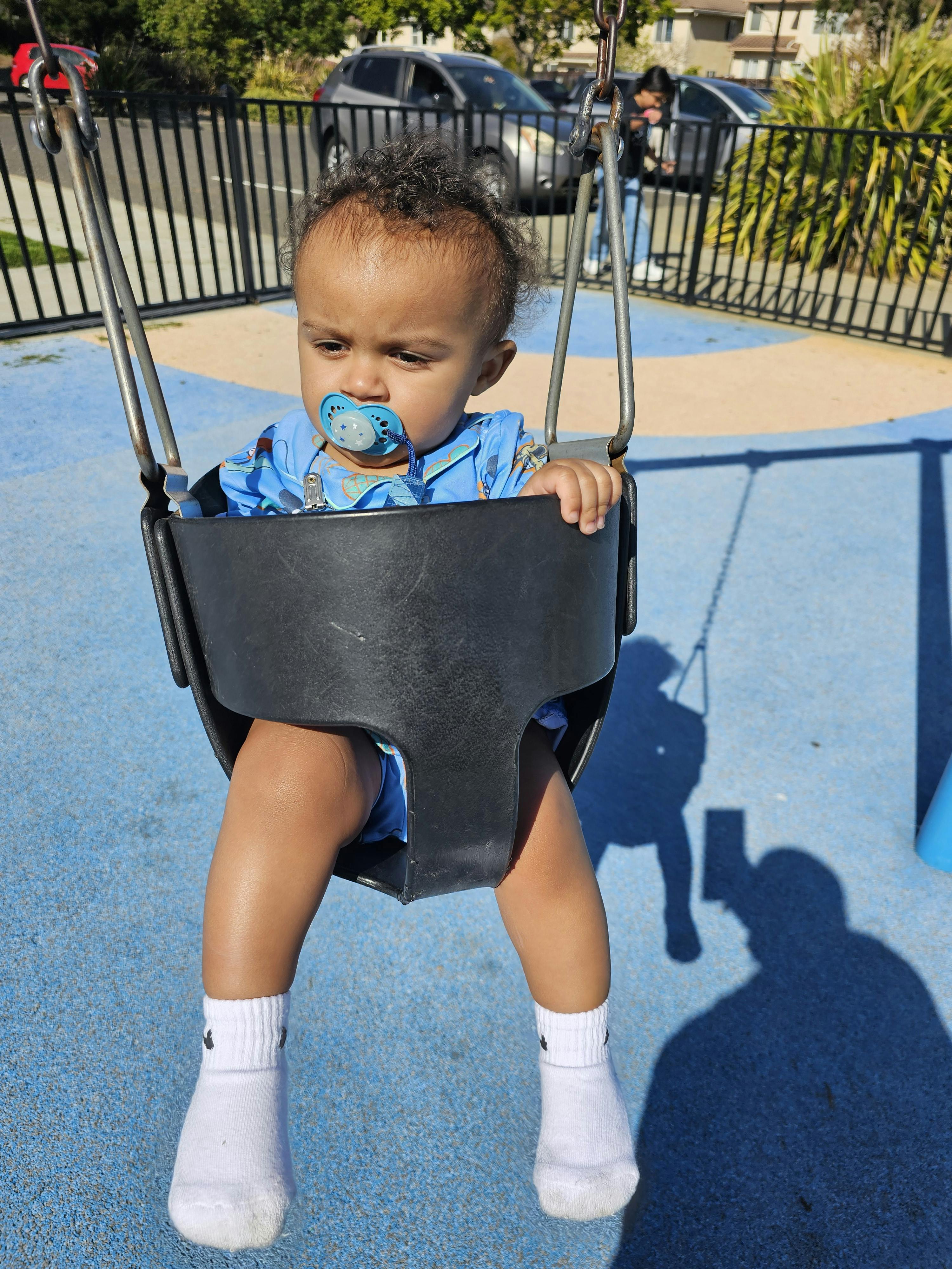 Child with a pacifier in a swing at a playground