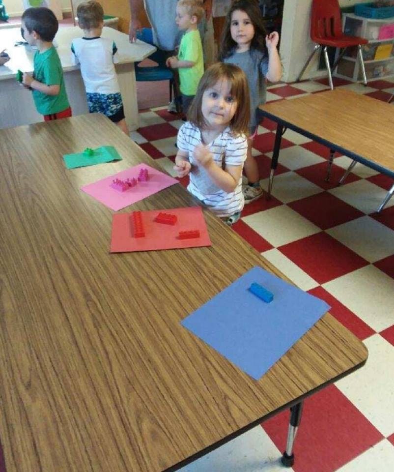 Child standing by a table with colorful papers and blocks in a classroom