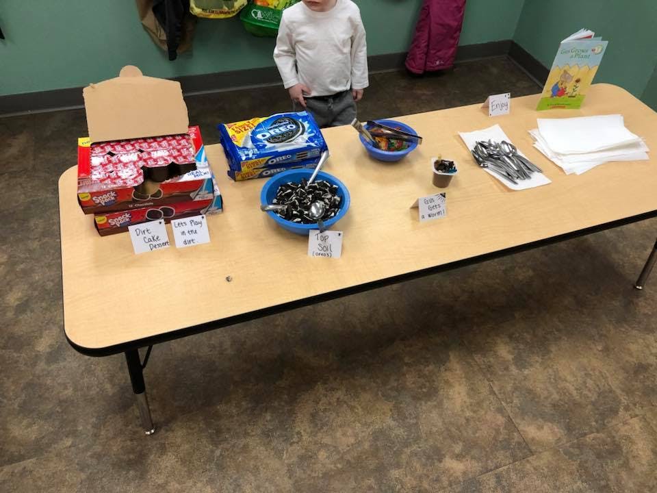 Child standing behind a table with snacks, cookies, and utensils