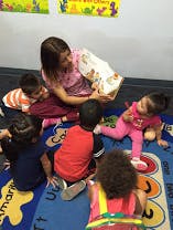 Adult reading a book to multiple children sitting on a mat