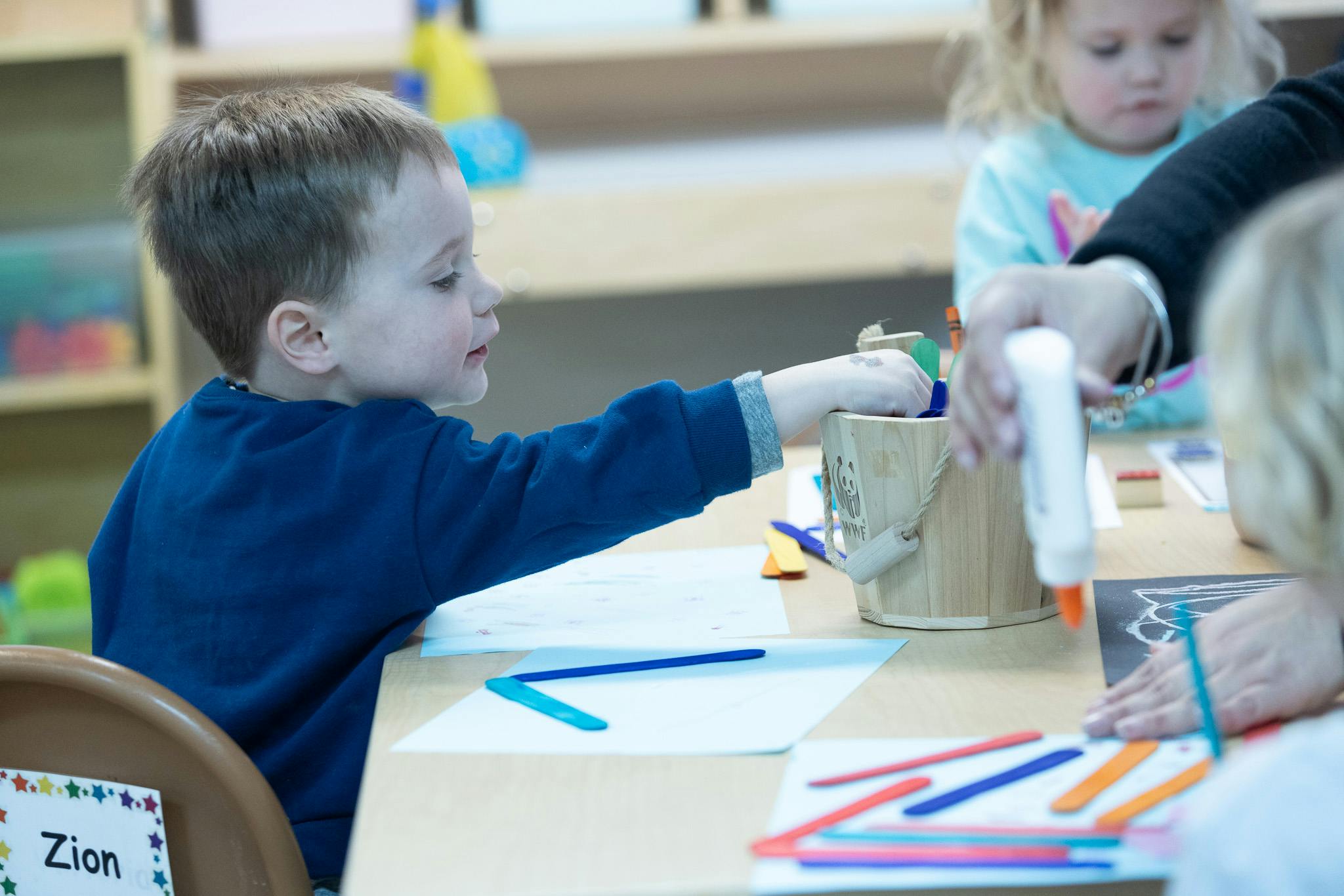 Child reaching for craft supplies at a table