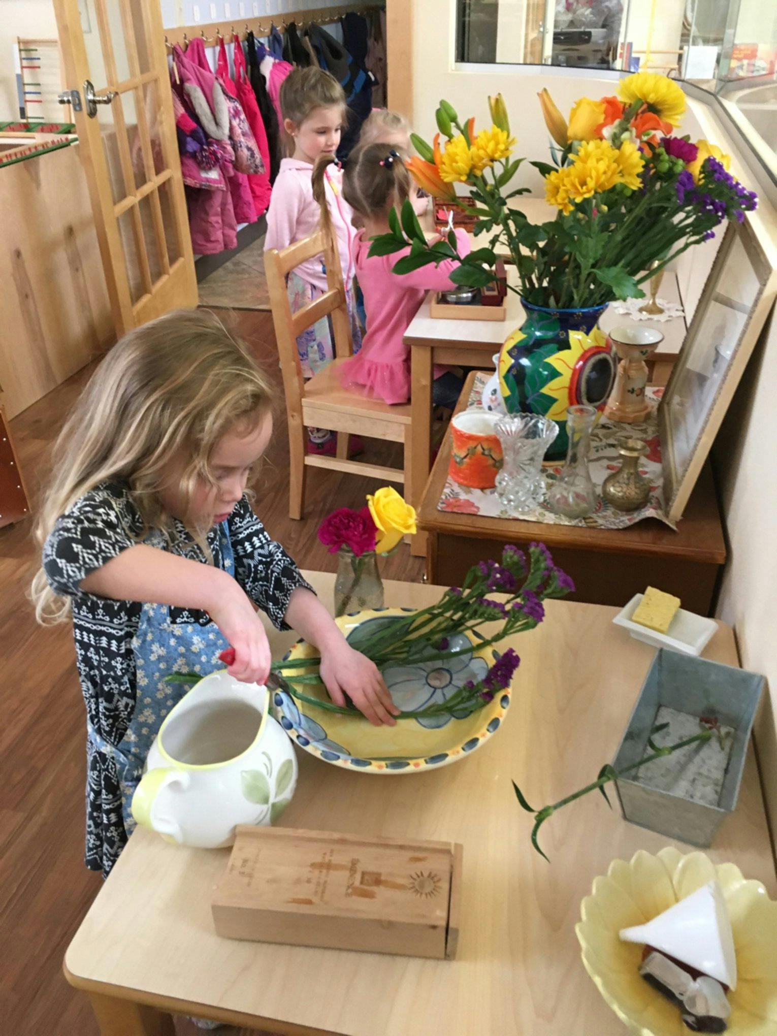 Child arranging flowers in a bowl with other children in the background