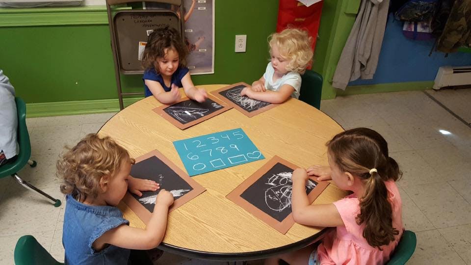 Four children drawing on chalkboards at a round table