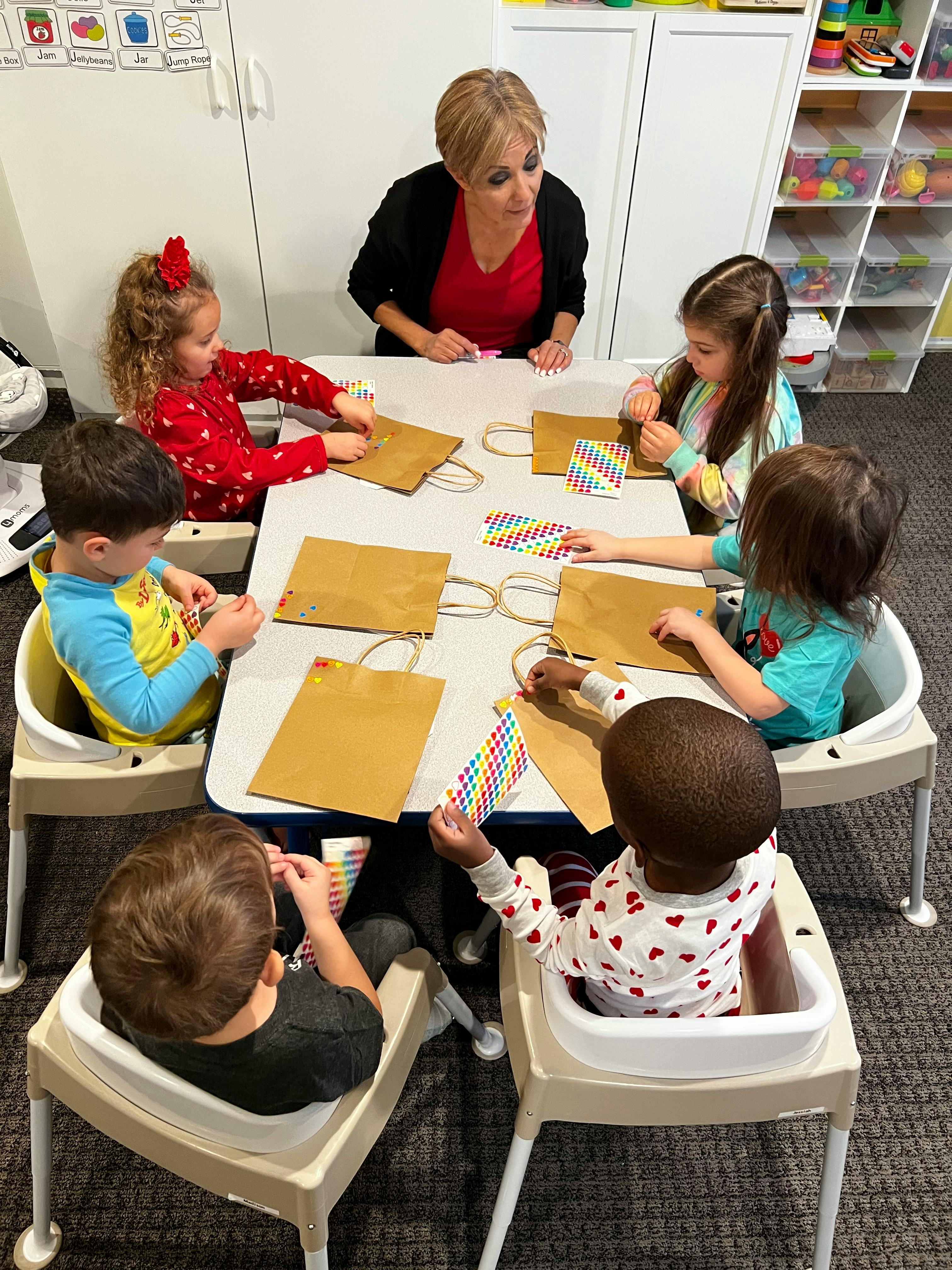 Adult and multiple children sitting at a table with craft bags and paper bags