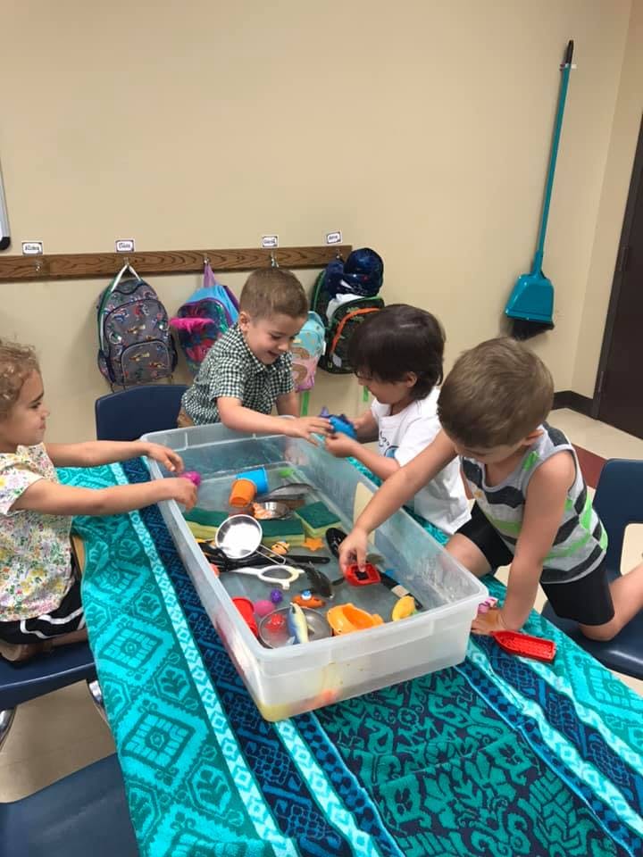 Four children playing with toys in a water table
