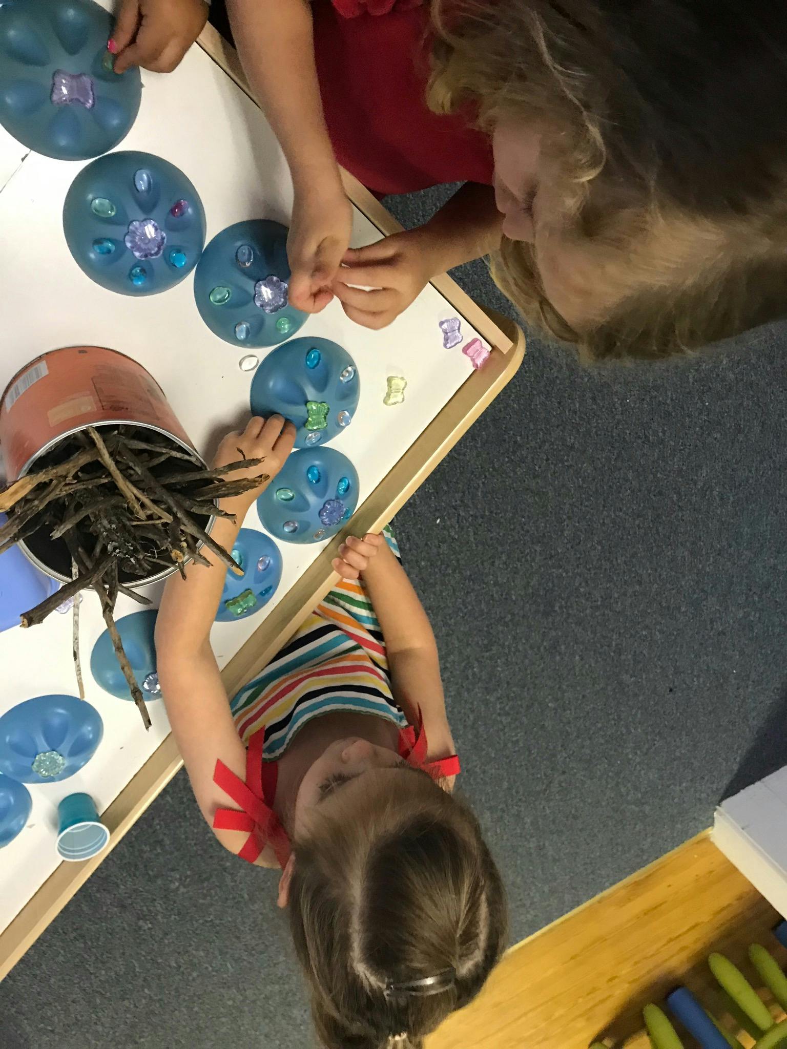 Two children playing with blue molds and small colorful objects on a table