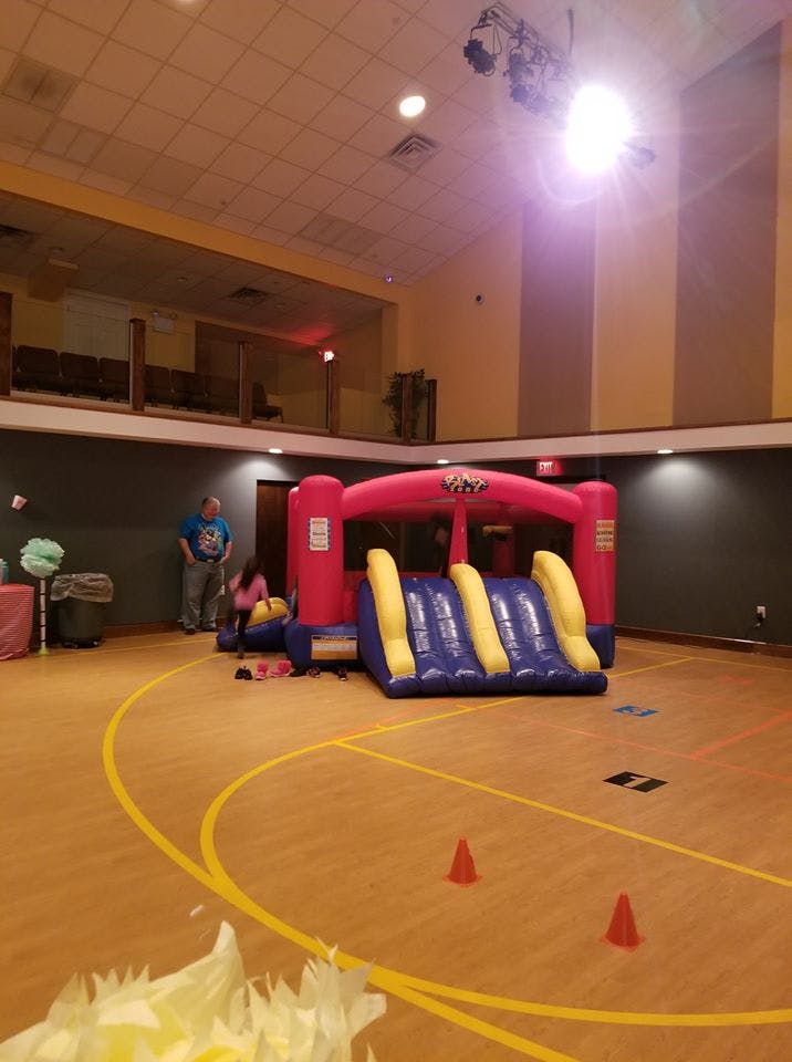 Inflatable bounce house and slide in a large room with a person standing nearby