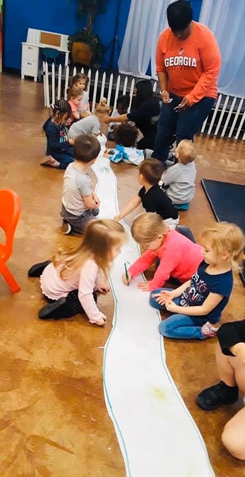Adult and multiple children sitting on the floor drawing on a long piece of paper