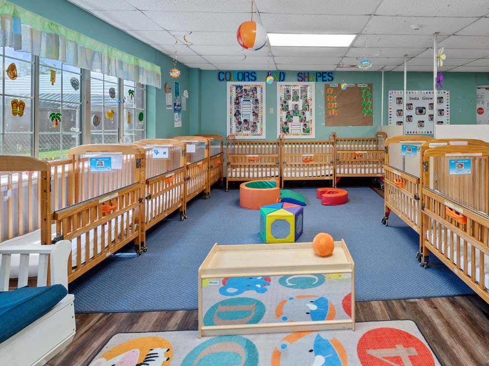 A brightly lit nursery room with multiple wooden cribs and colorful play items