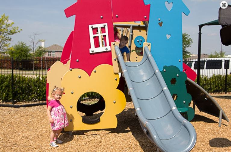 Child standing next to a colorful playground structure with a slide