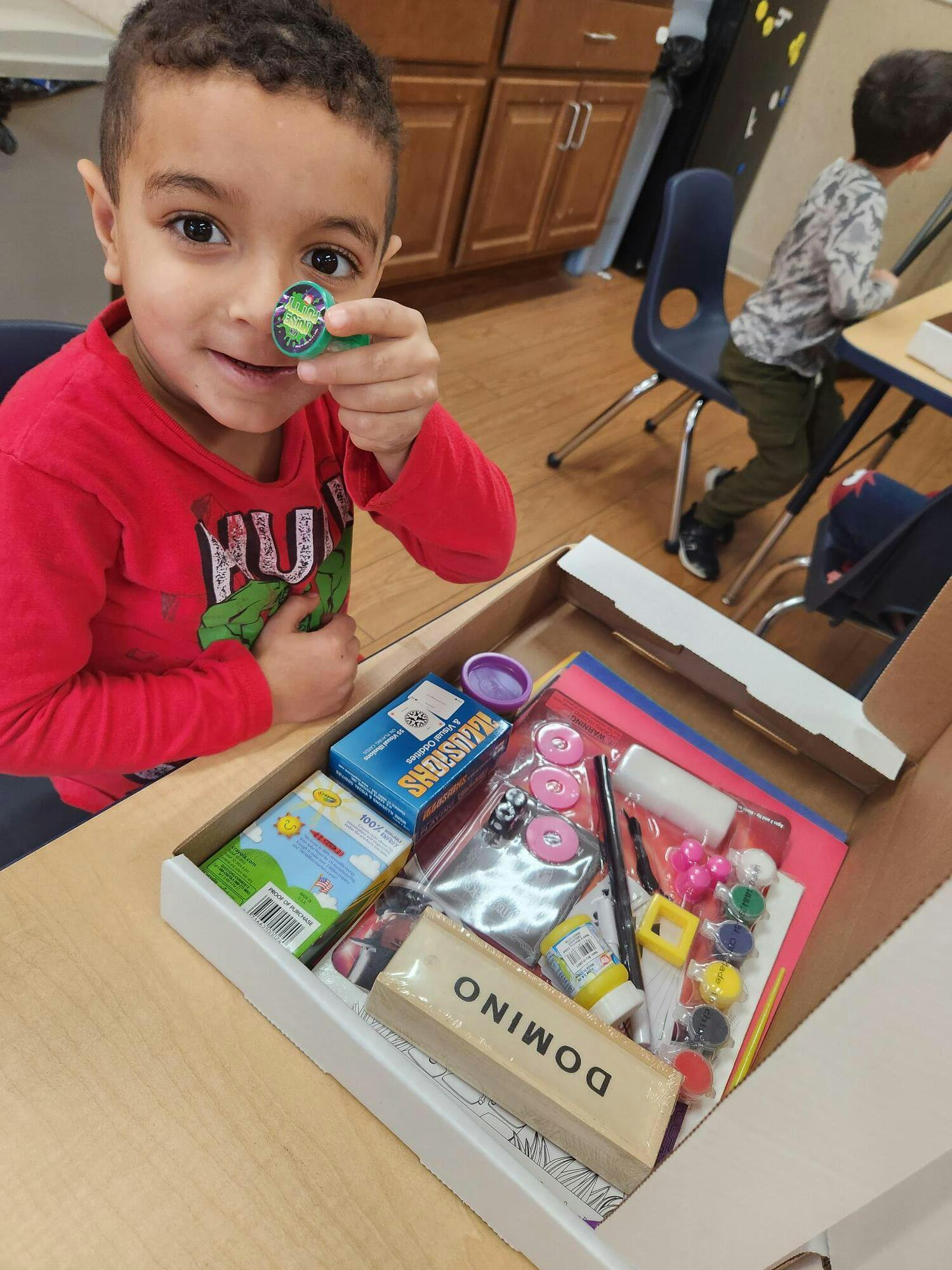 Child holding a small toy up to their eye, looking into a box of supplies
