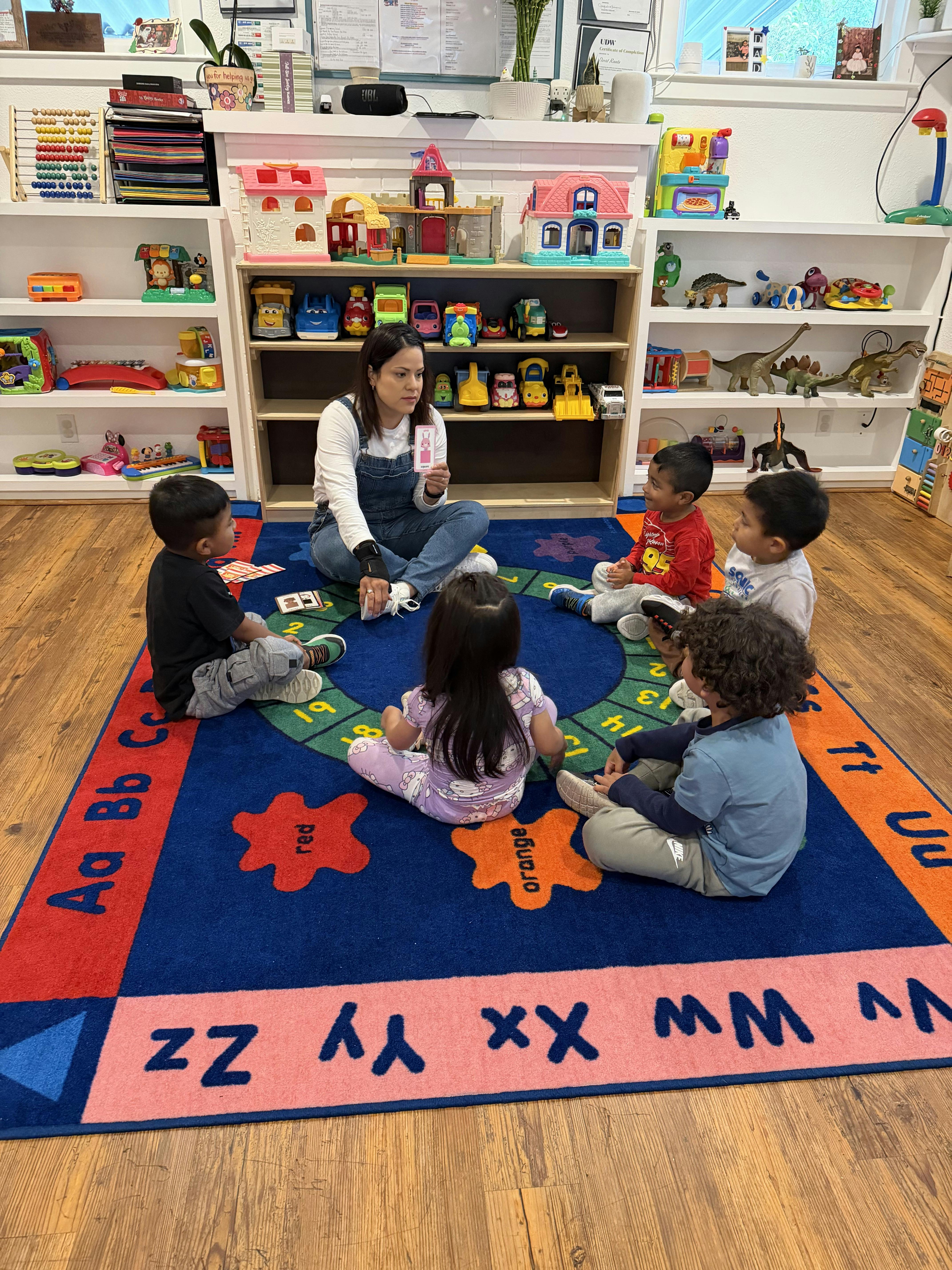 Adult and several children sitting on a rug with letters and colors on it
