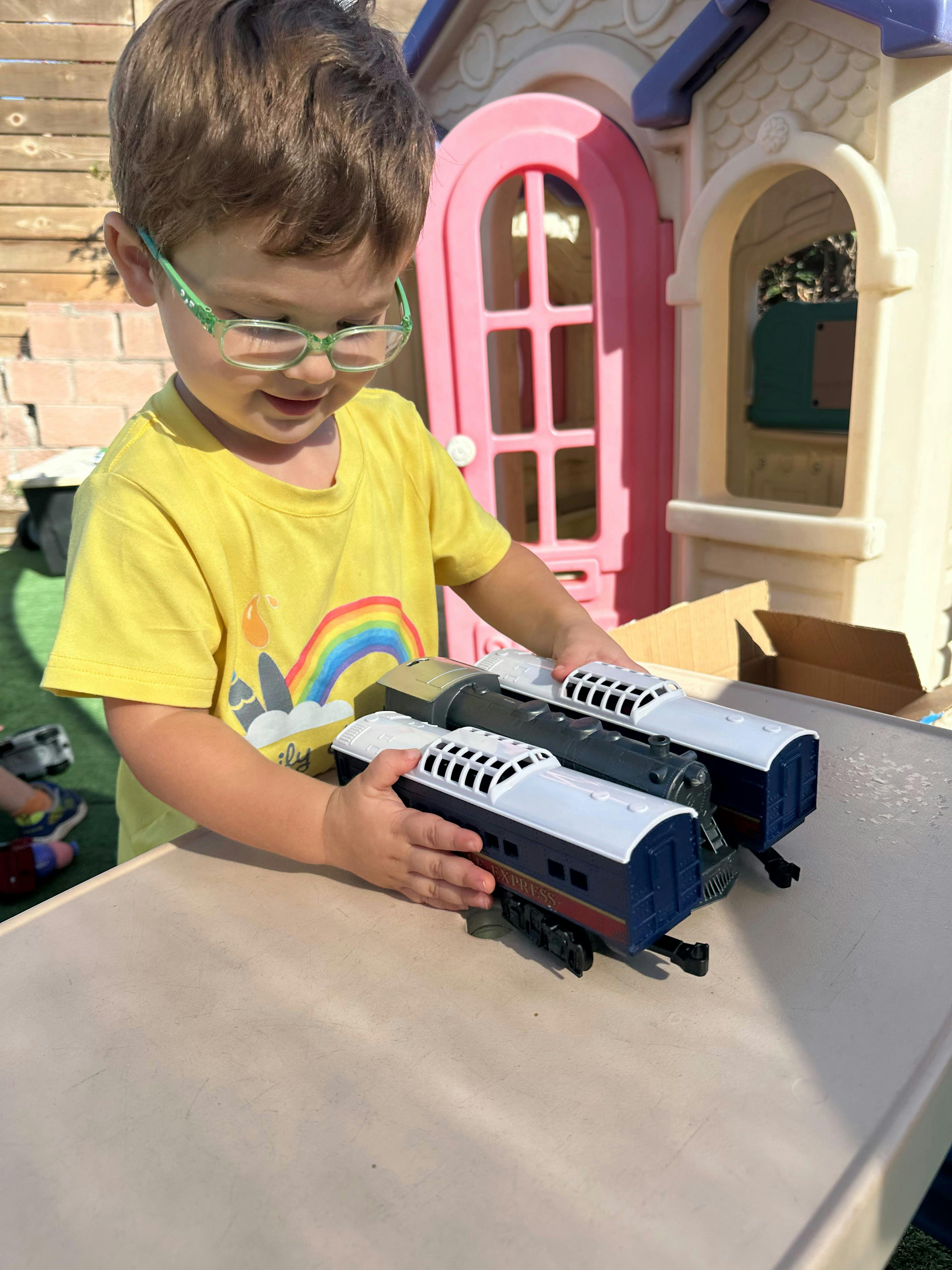 Child playing with a toy train set on a table outdoors