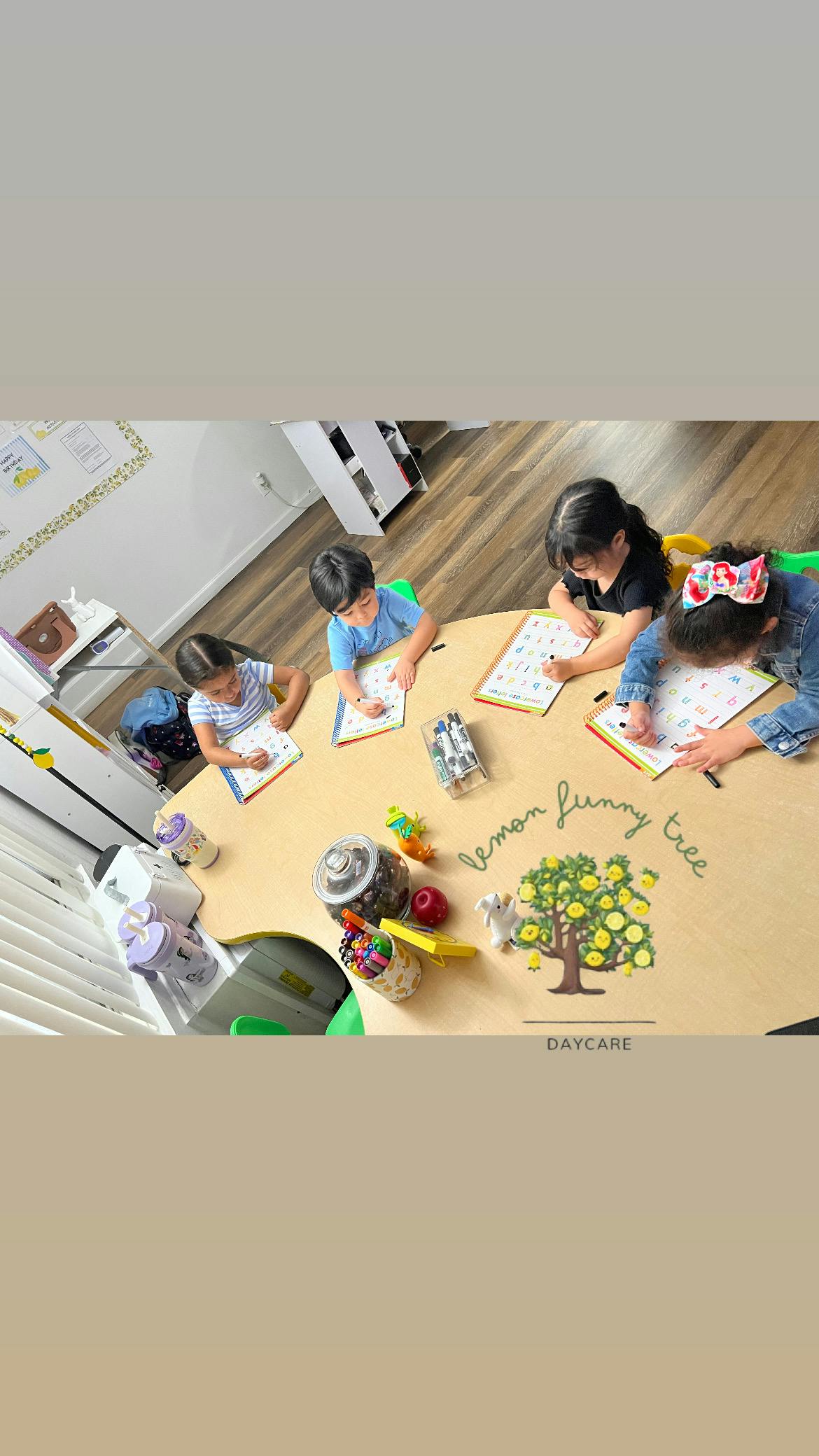 four children sitting at a round table, tracing letters in workbooks