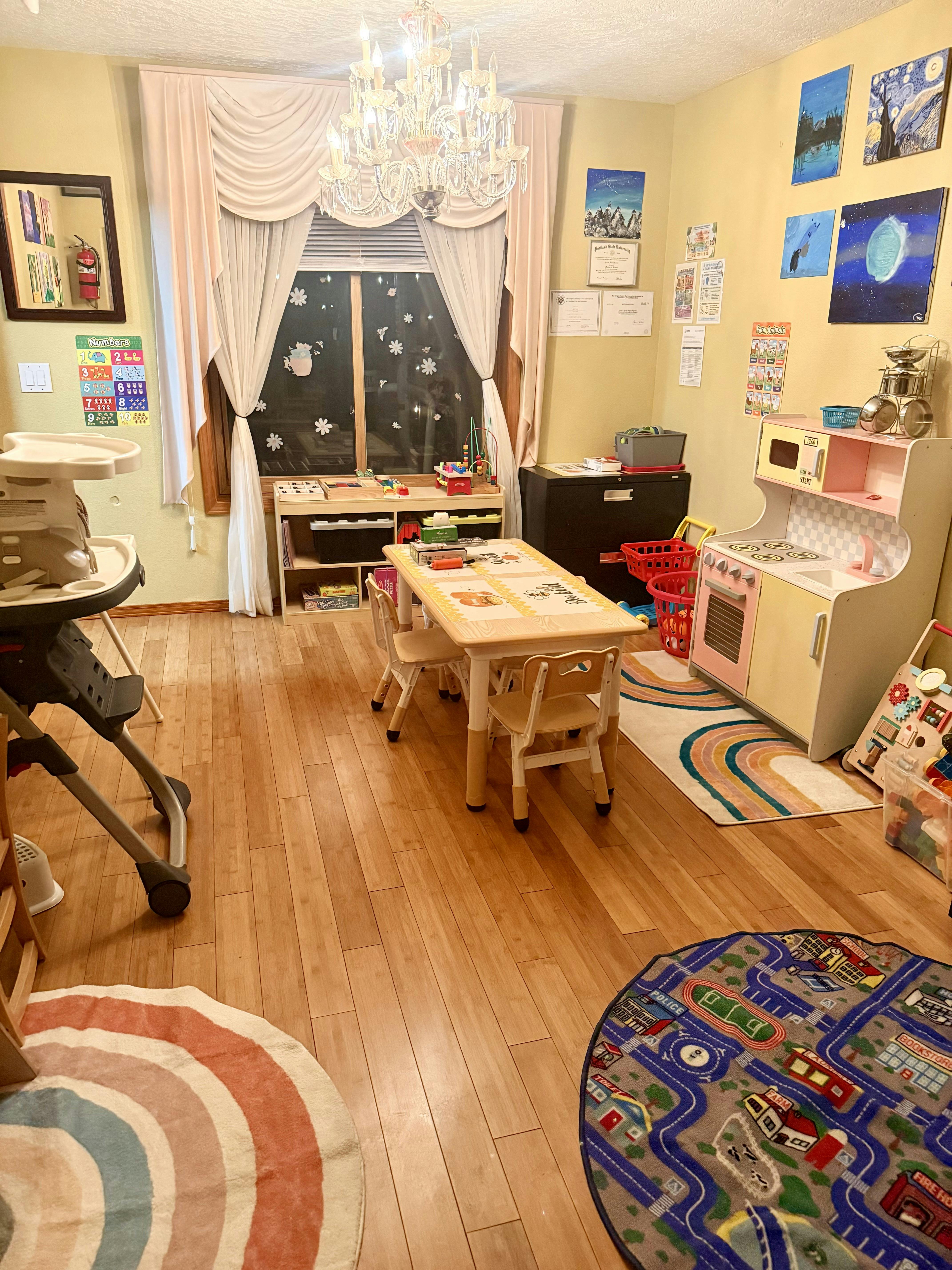 Childcare room with a play kitchen, table for children, and play rugs