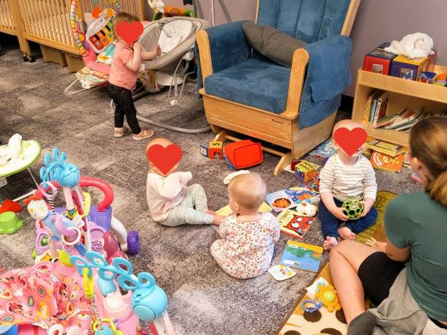 A person sitting with several small children playing with toys on a carpeted floor
