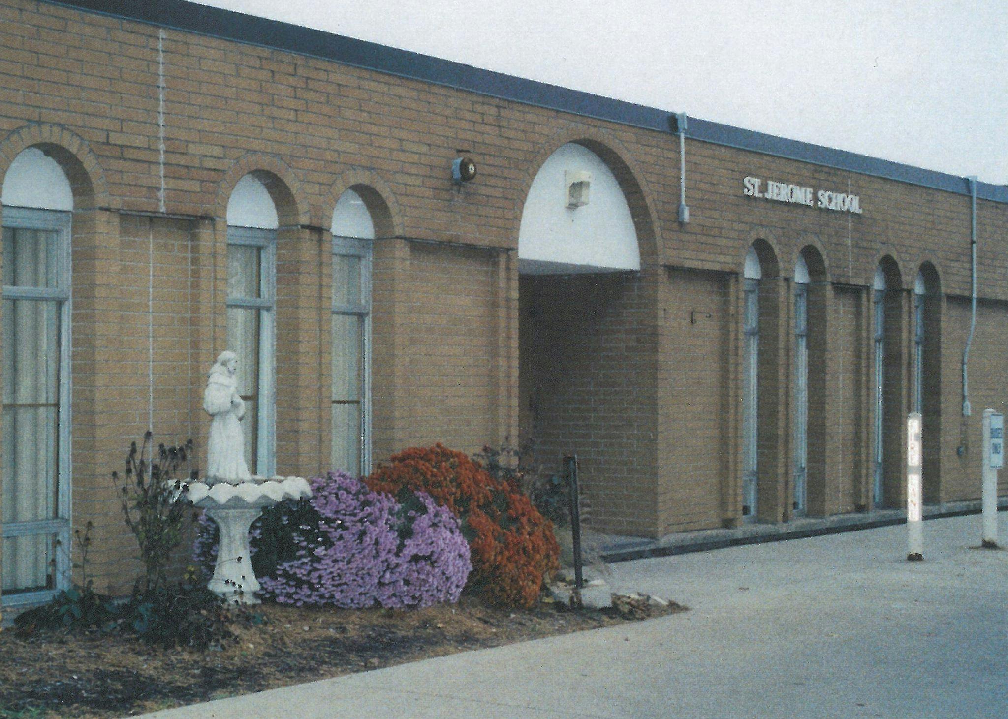 Brick school building with an archway entrance, a statue in a planter, and "ST. JEROME SCHOOL" on the wall
