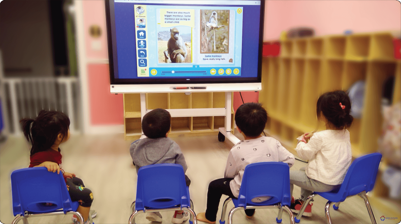 Four children sitting on chairs watching a large screen in a classroom