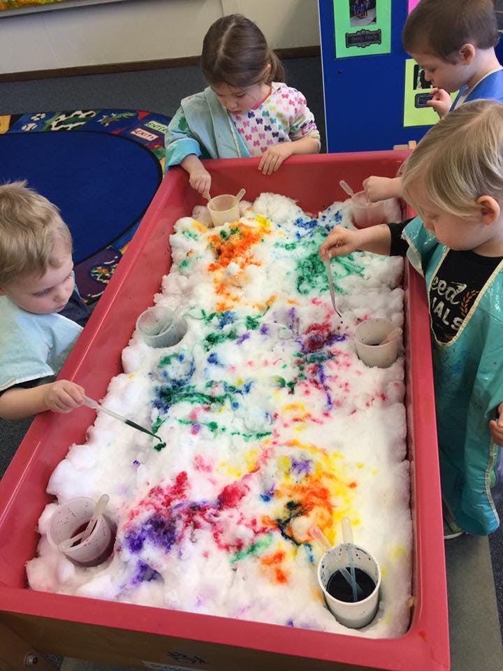 Children playing with colorful foam in a red sensory bin