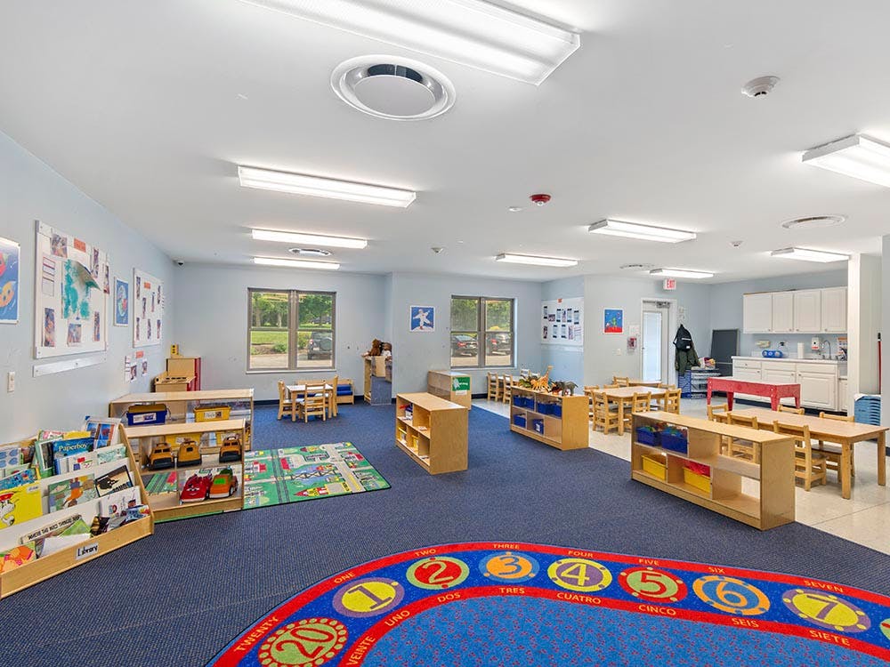 Classroom with children's tables and chairs, bookshelves, and colorful rug