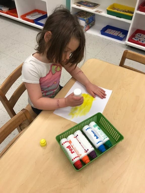Child painting with a yellow paint stick at a table
