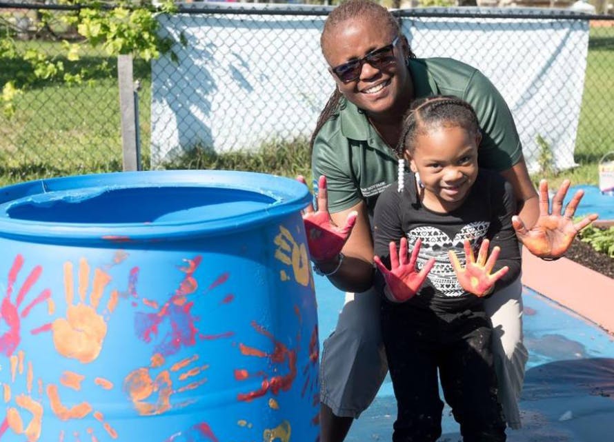 Person and child showing hands covered in paint next to a painted barrel