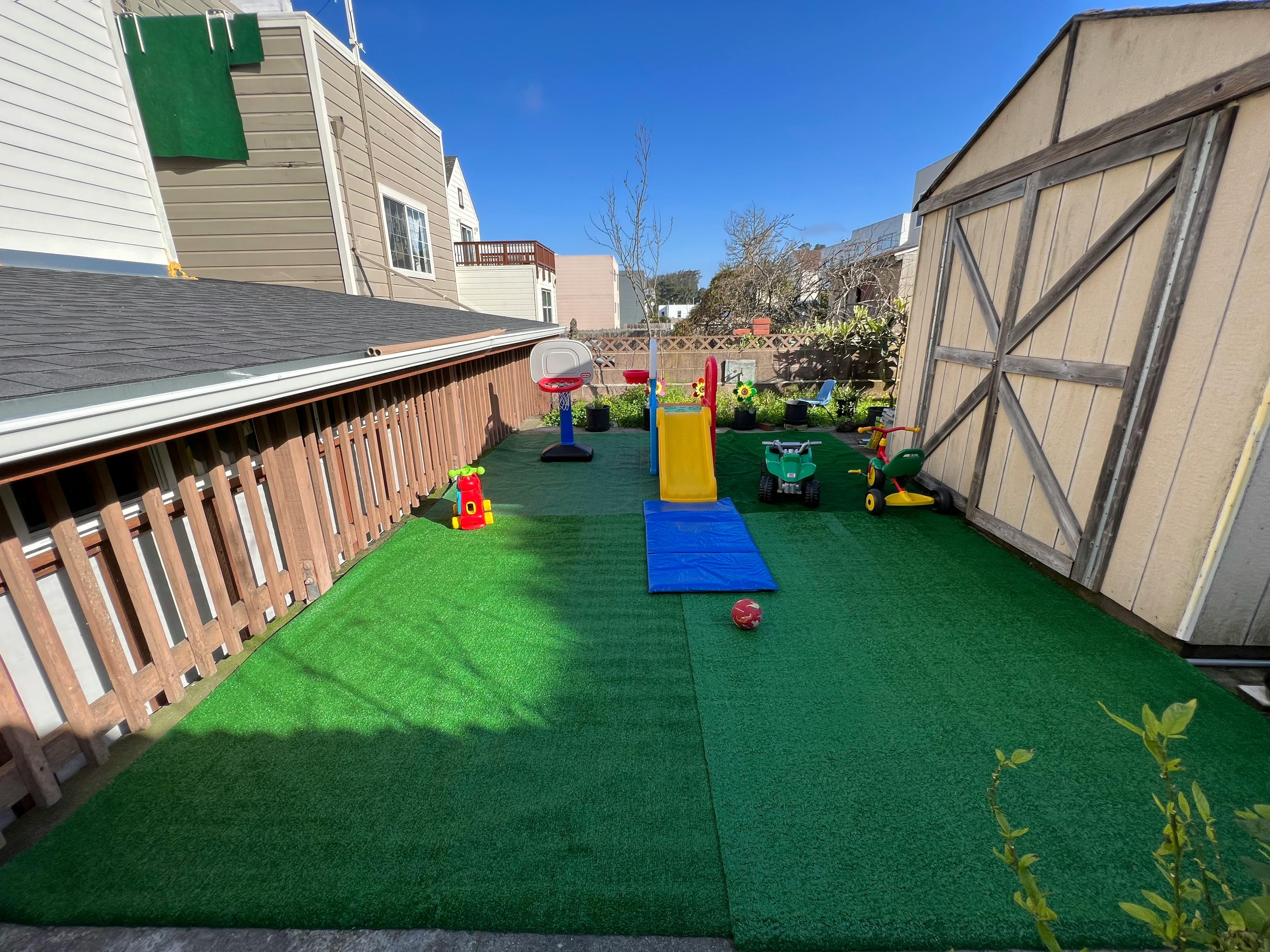 Backyard with artificial turf, play slide, and basketball hoop