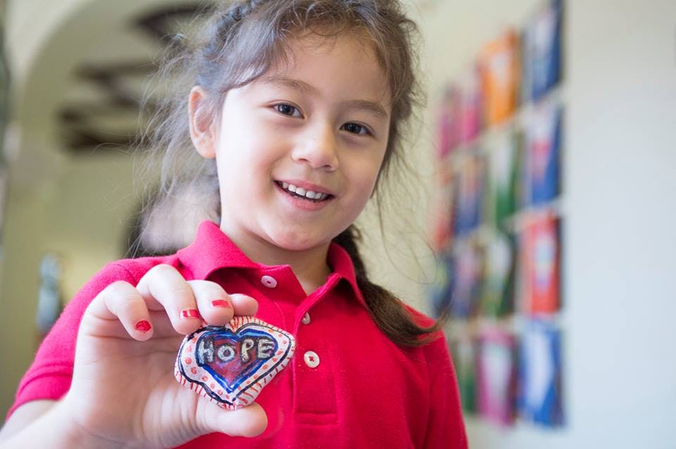 Child holding up a heart-shaped object with the word HOPE on it