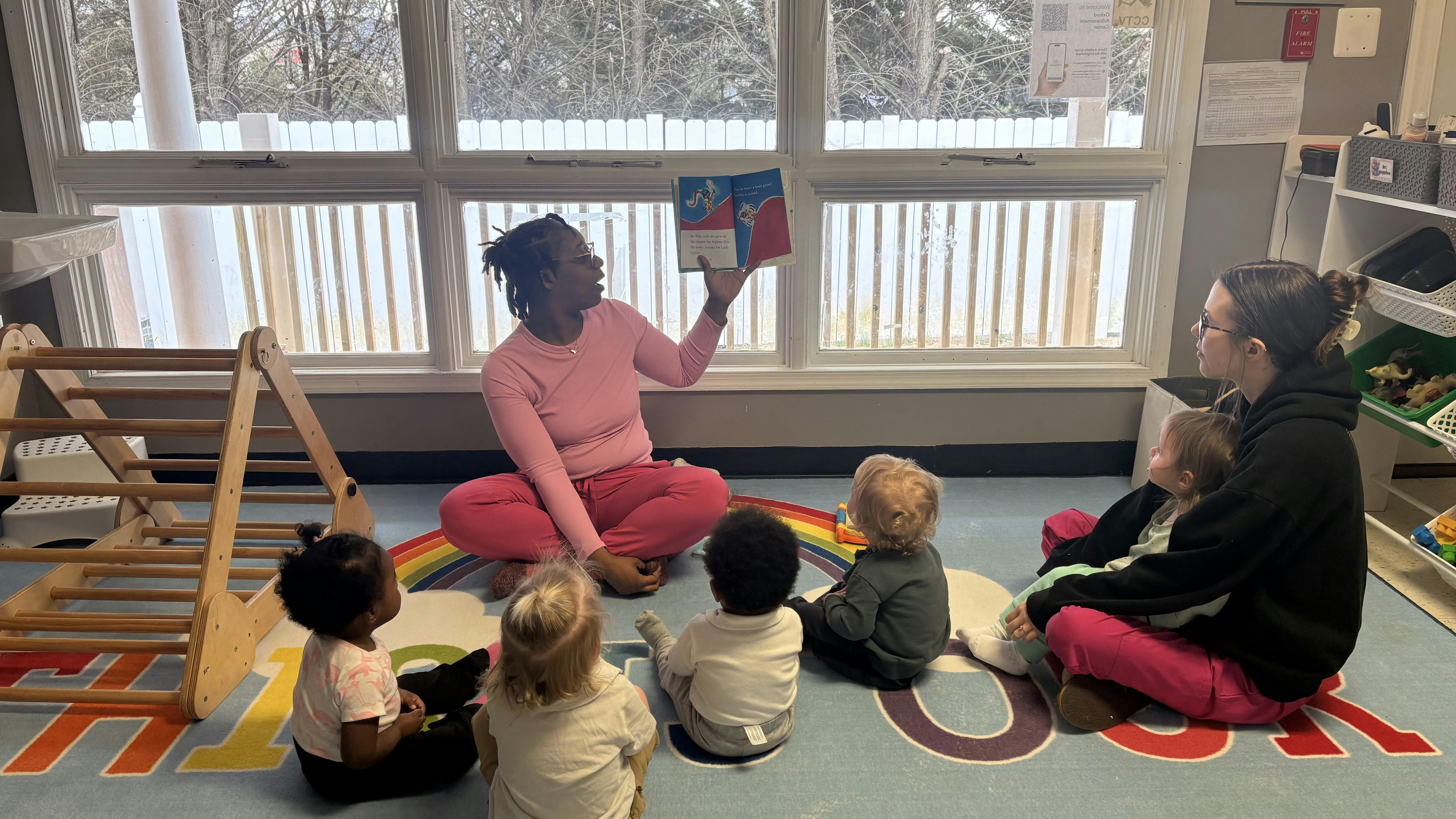 Person reading a book to four children and one adult in a classroom
