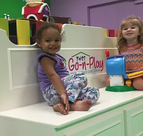 Two children sitting on a white bench with a "Go-n-Play" sign behind them