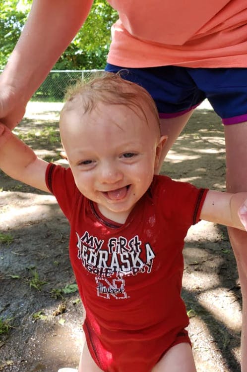 Child in red shirt with text "My First Nebraska" being held by an adult