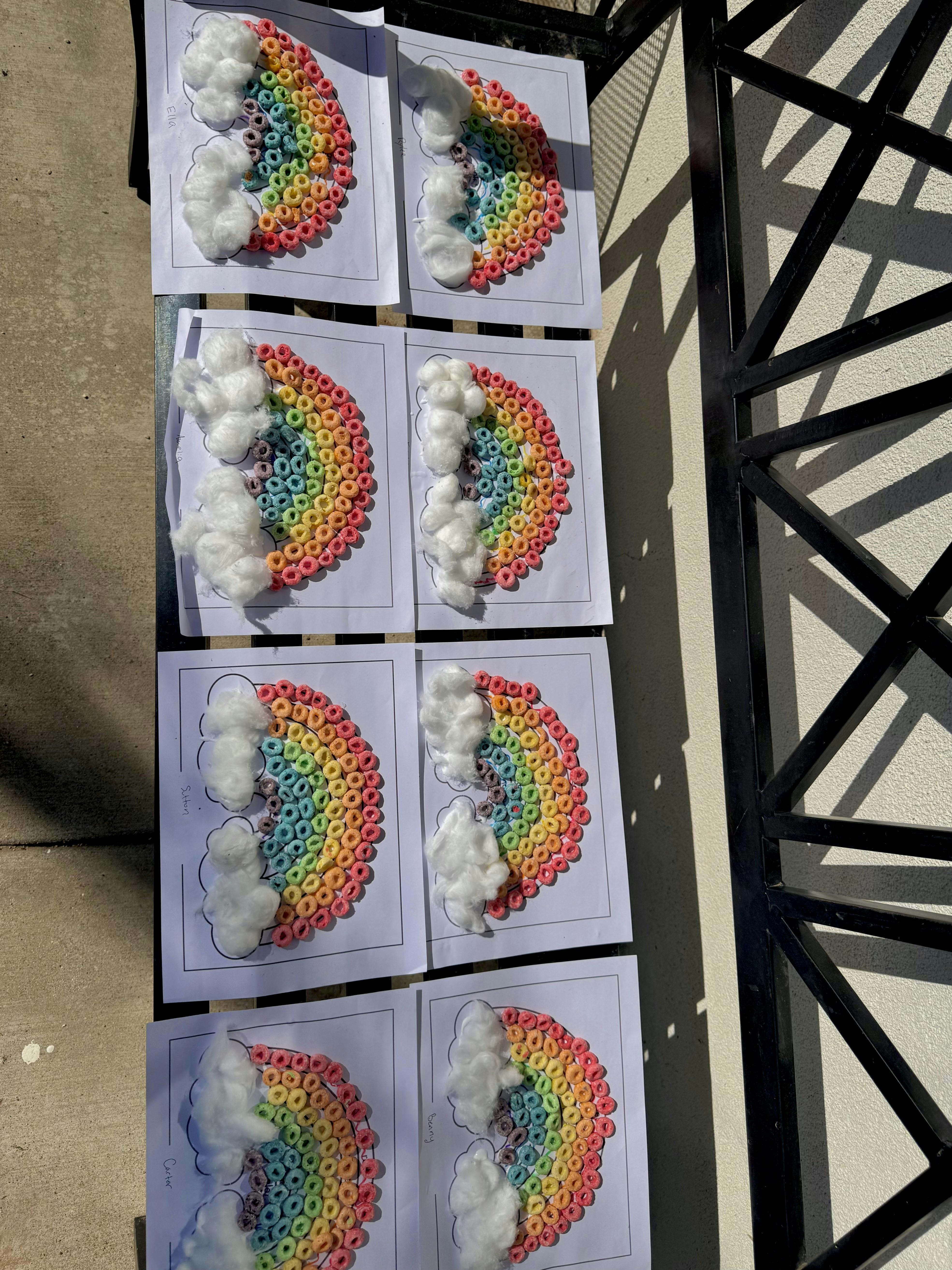 Cereal and cotton ball rainbow crafts on paper arranged on a bench