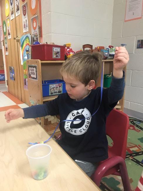Child sitting at a table, holding a string with beads