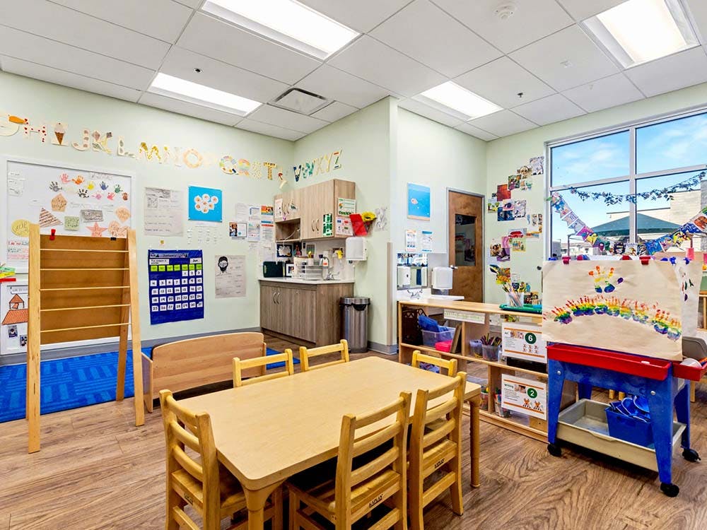 Classroom with tables, chairs, colorful wall decorations, and a children's easel