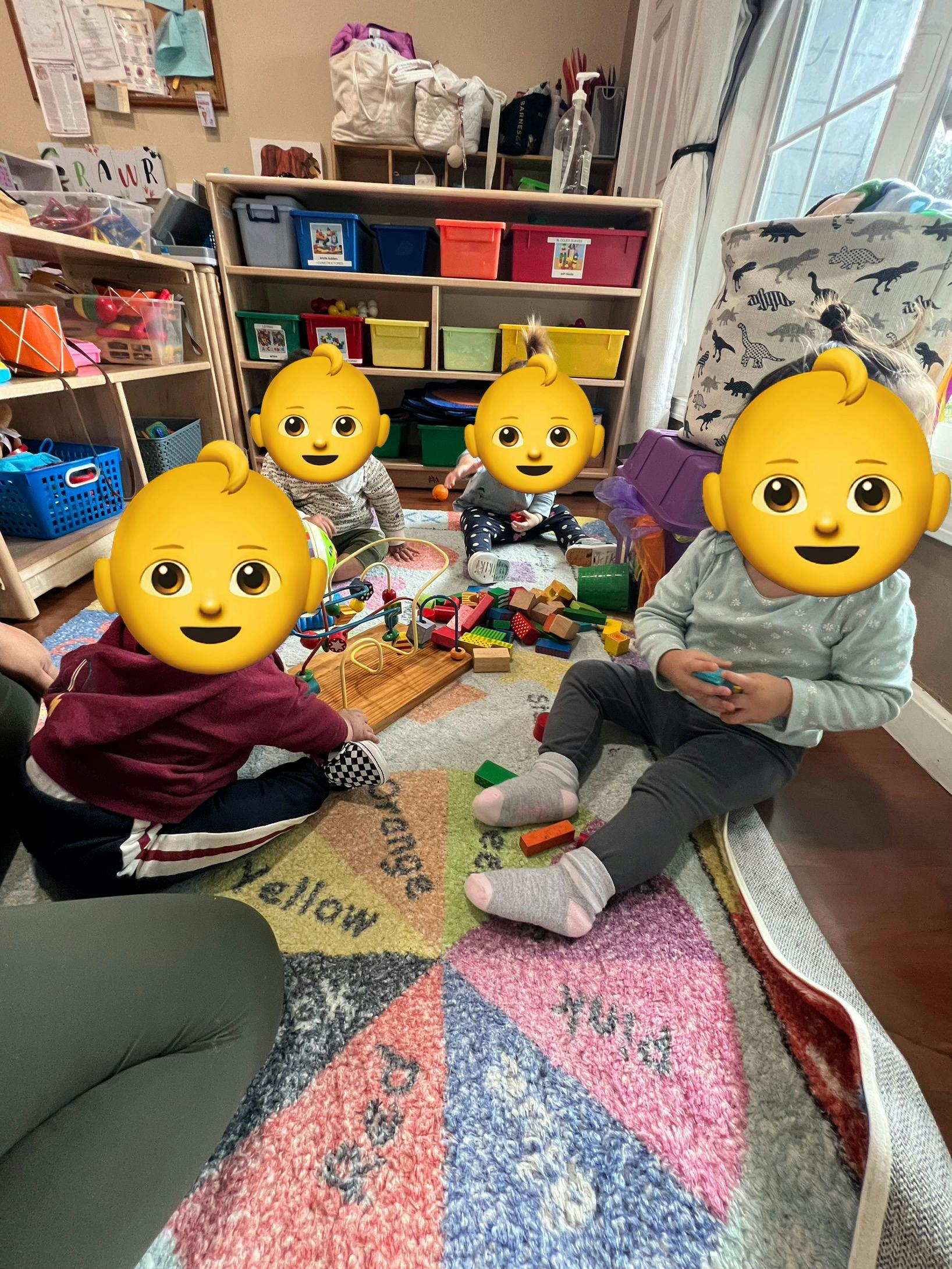 Four children playing on a colorful rug in a room with shelves