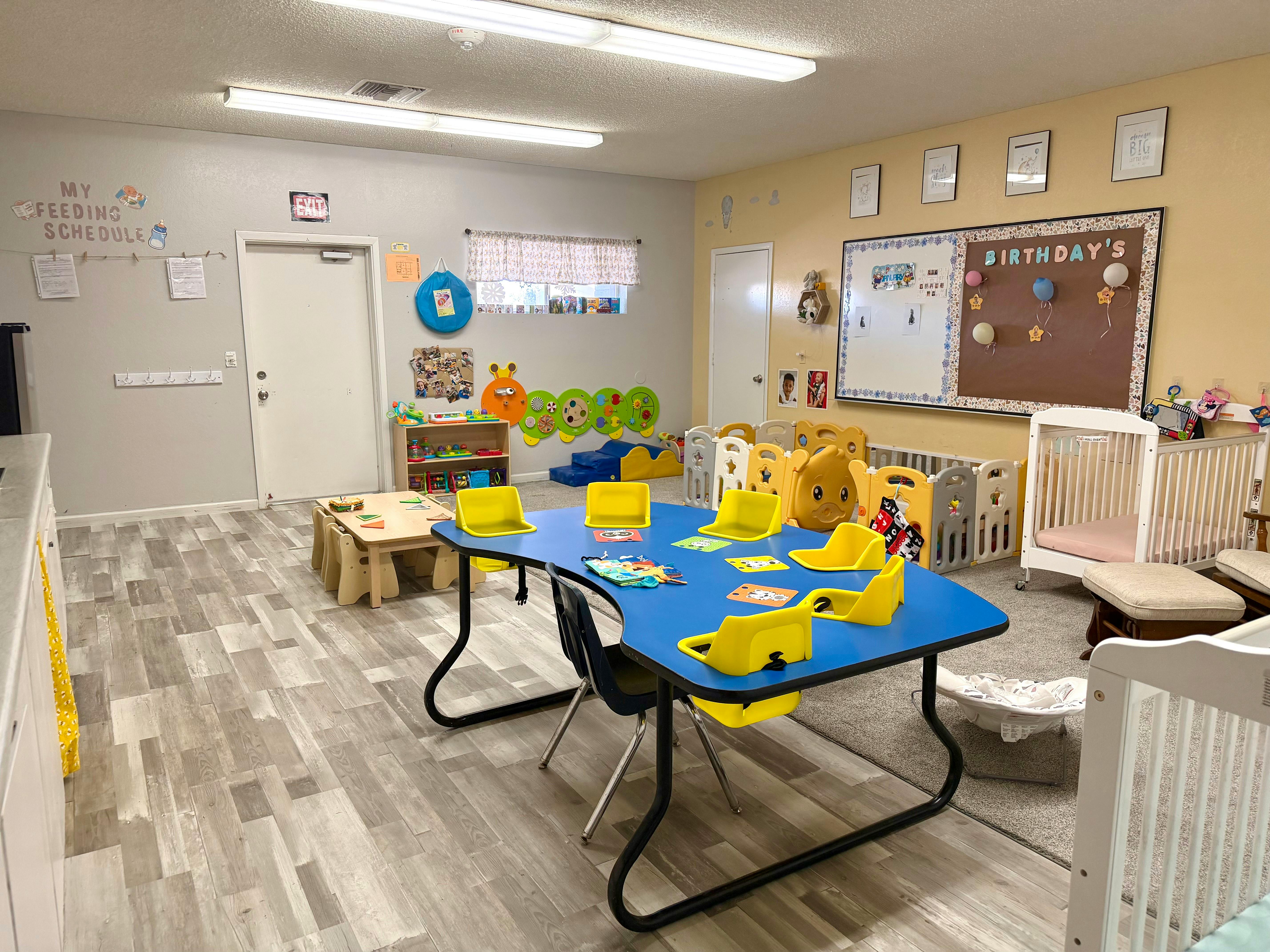 A colorful classroom with child-sized tables, chairs, playpens, and cribs