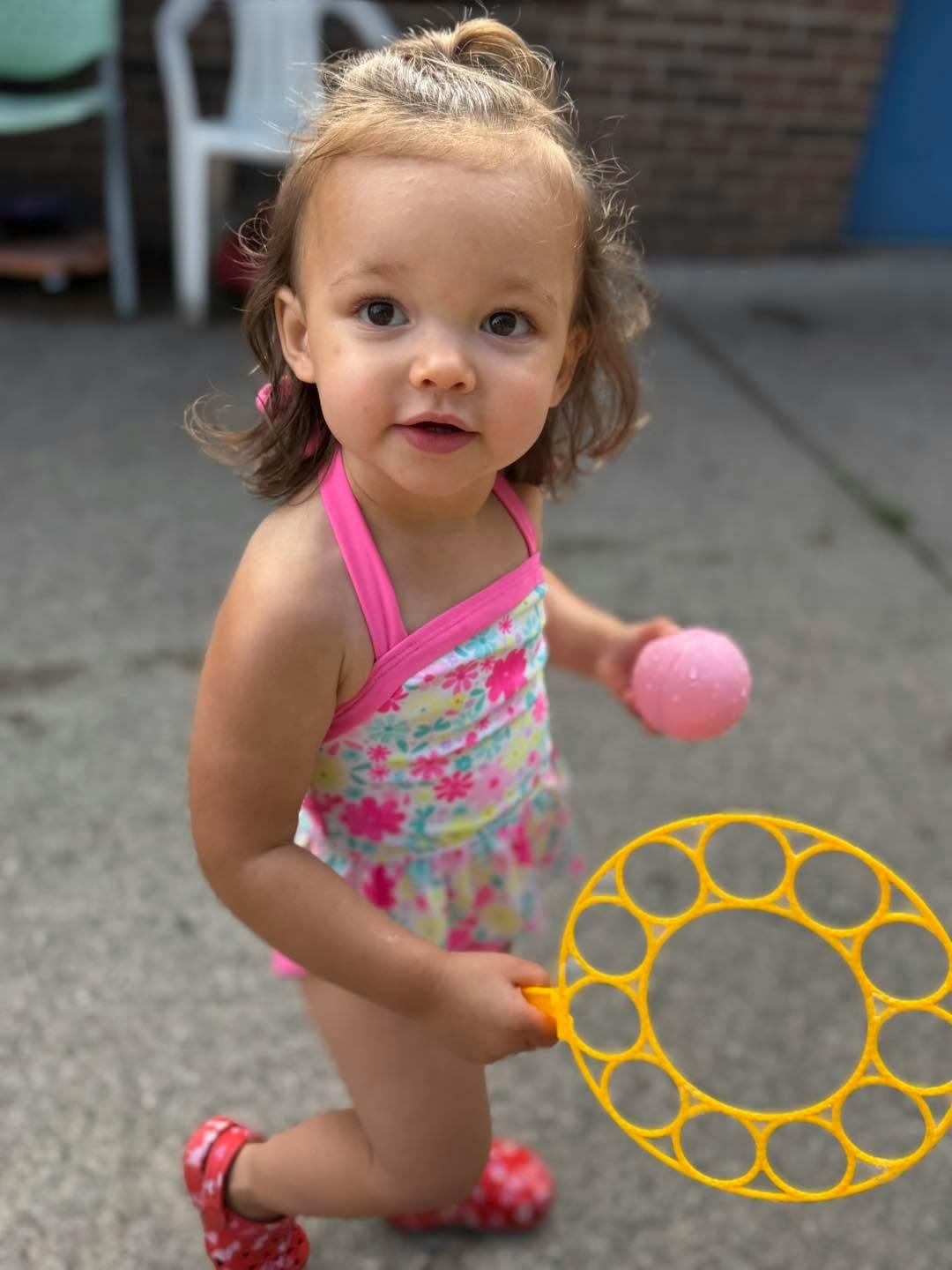 Child wearing a swimsuit holding a bubble wand and a small ball