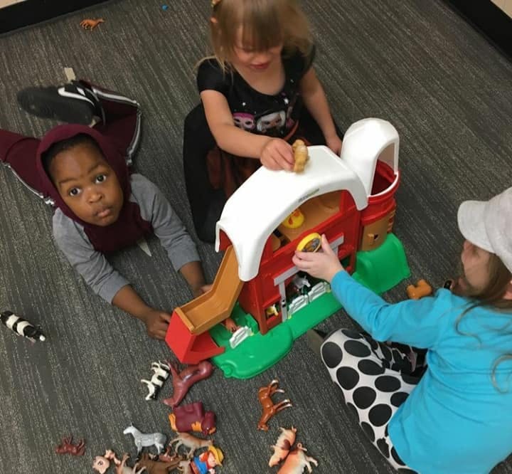 Three children playing with a toy farm set on the floor