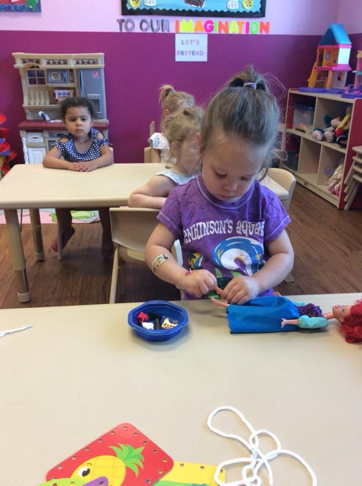 Child playing with a doll at a table in a classroom