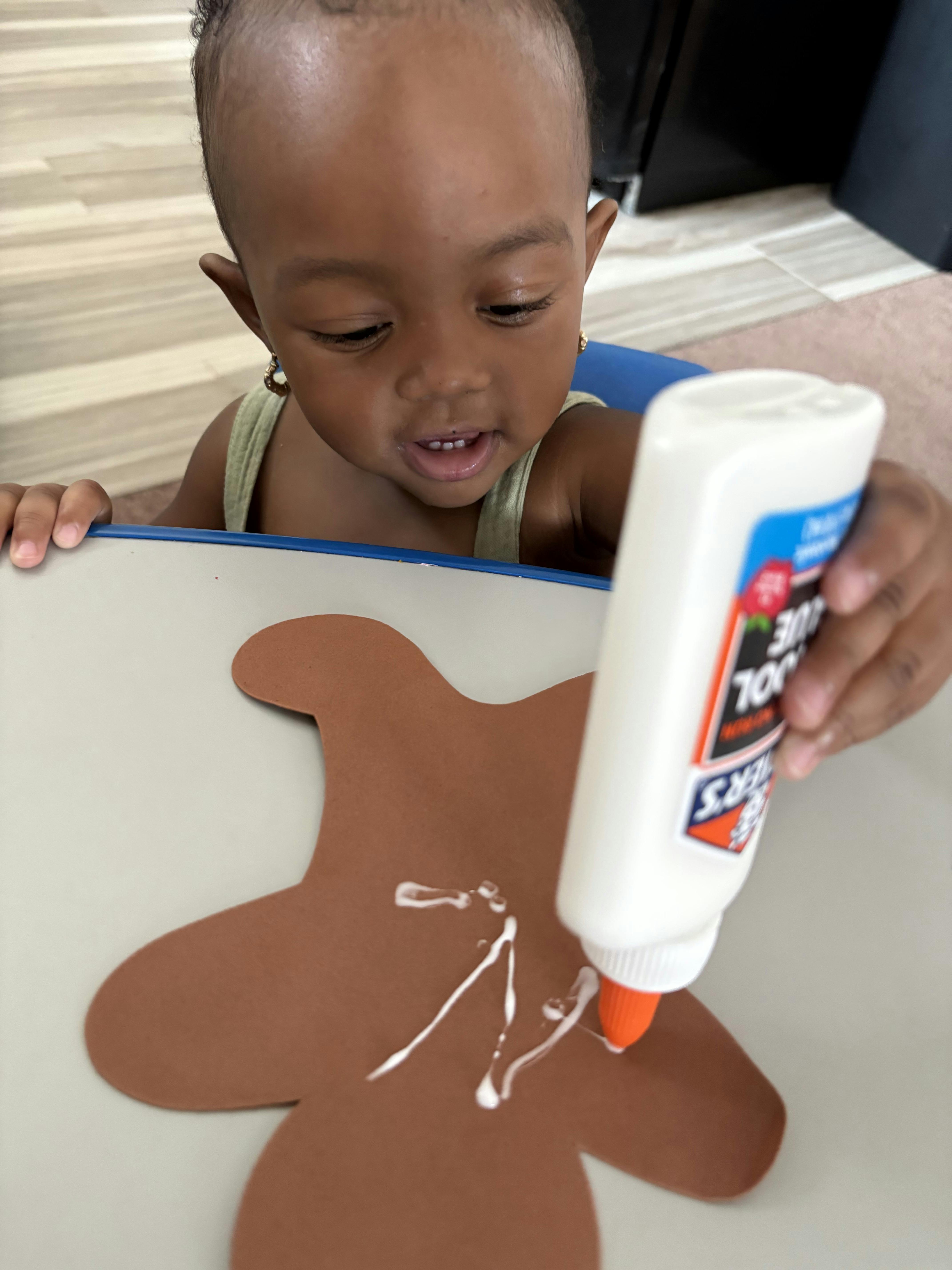 Child applying glue to a brown paper cutout