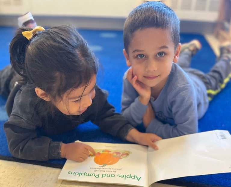 Two children lying on a blue rug reading the book Apples and Pumpkins
